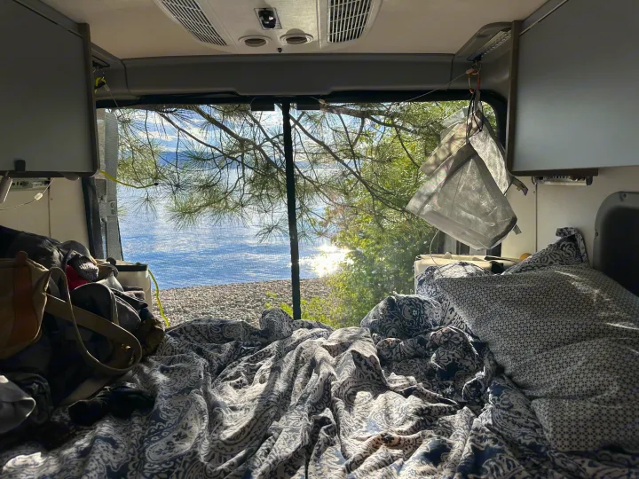 Cozy rv rental bed offers a stunning lake view from inside the camper van, screen allowing fresh air. Ideal for travel.. Winnebago Solis 2022