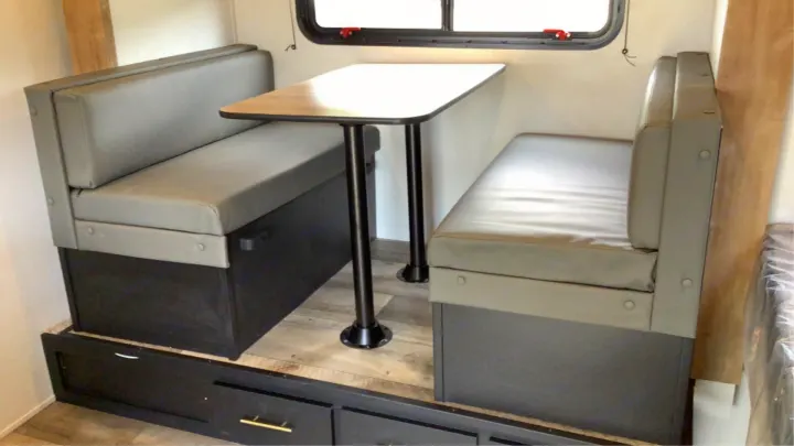 RV rental dinette: gray cushioned benches, light table, window above. Includes lower storage drawers for convenience.. Keystone RV Springdale 2023