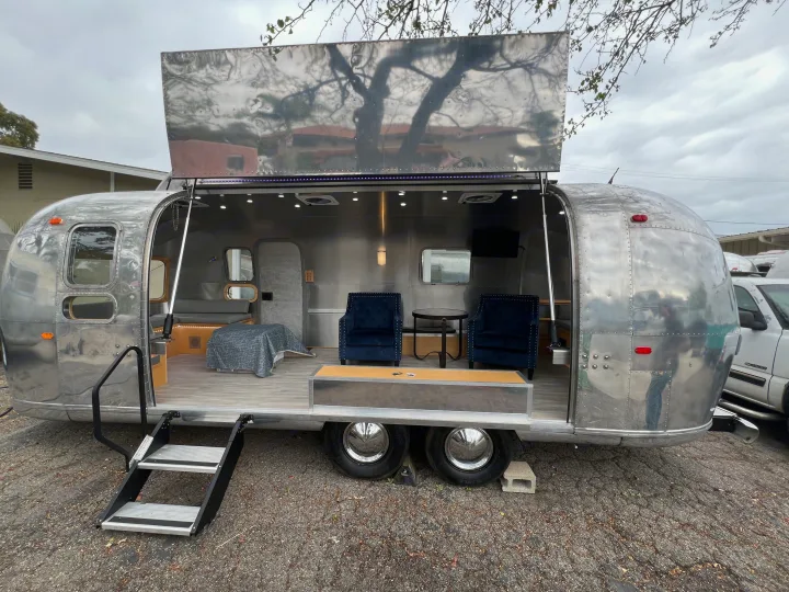 Modern rv rental: a polished silver travel trailer with an open side showing a cozy lounge interior and steps.. Airstream Airstream 1971