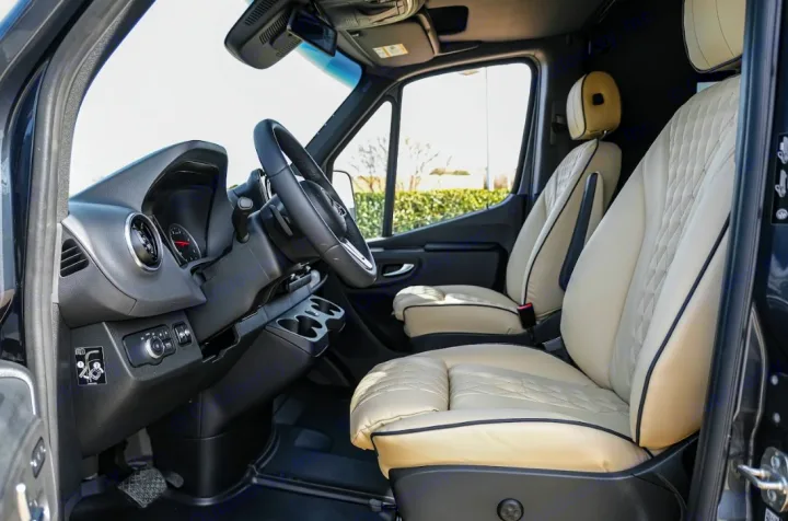 Modern RV rental front cabin with comfortable cream quilted leather seats, dashboard, and steering wheel visible.. Mercedes Benz Executive Lounger by Legends Sprinter 3500XD 170 2023