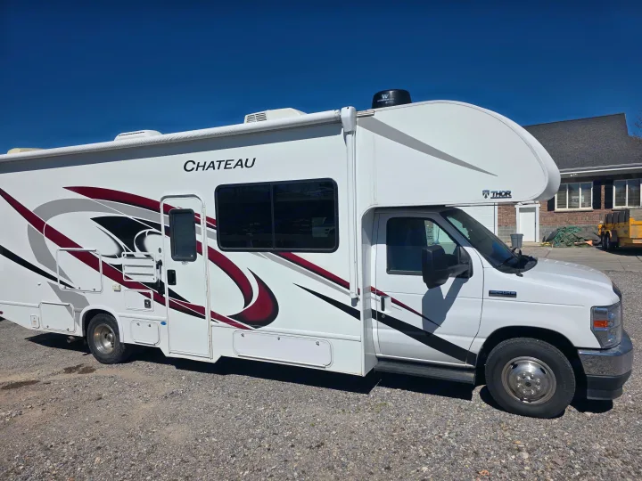 White Thor Chateau Class C RV rental motorhome with graphic decals, parked on gravel. Your next adventure awaits!. Thor Chateau 2021