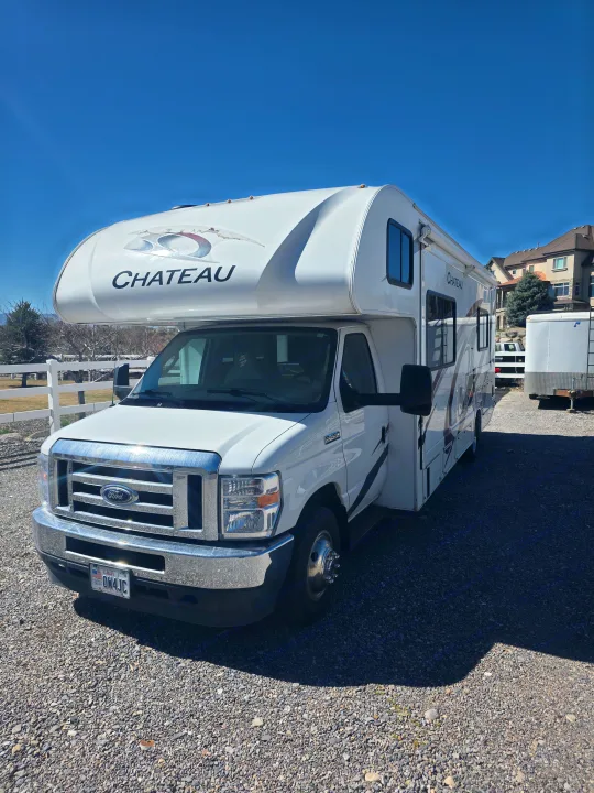 A white Ford Chateau RV is parked on a gravel lot under a clear blue sky, perfect for your next rv rental adventure.. Thor Chateau 2021