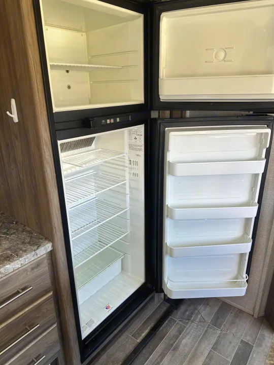 Clean, empty RV rental refrigerator and freezer, ready for your trip. Spacious fridge interior with shelves.. Crossroads RV Zinger 2021
