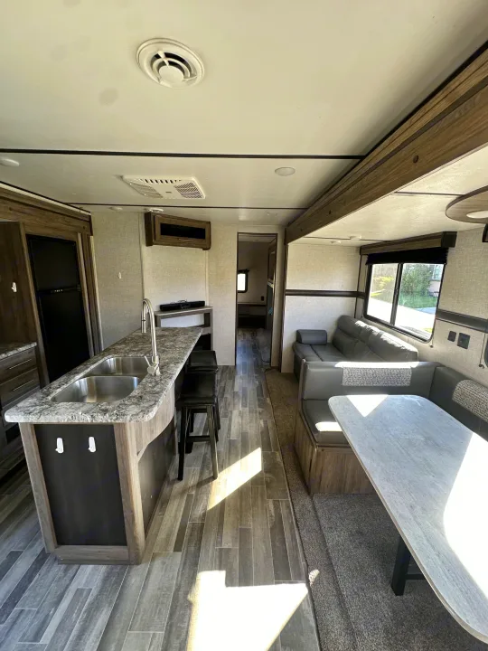 Spacious RV rental interior featuring a modern kitchen, dining booth, and sofa. Bright and clean, ready for travel adventures.. Crossroads RV Zinger 2021