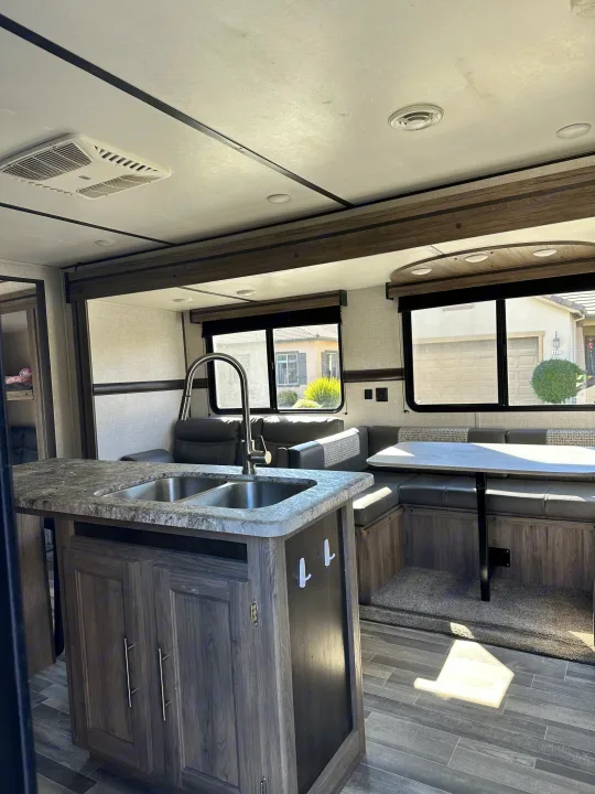 RV rental: Bright, modern interior featuring a kitchen island, dining booth, and sofa, with an AC unit and outside views.. Crossroads RV Zinger 2021