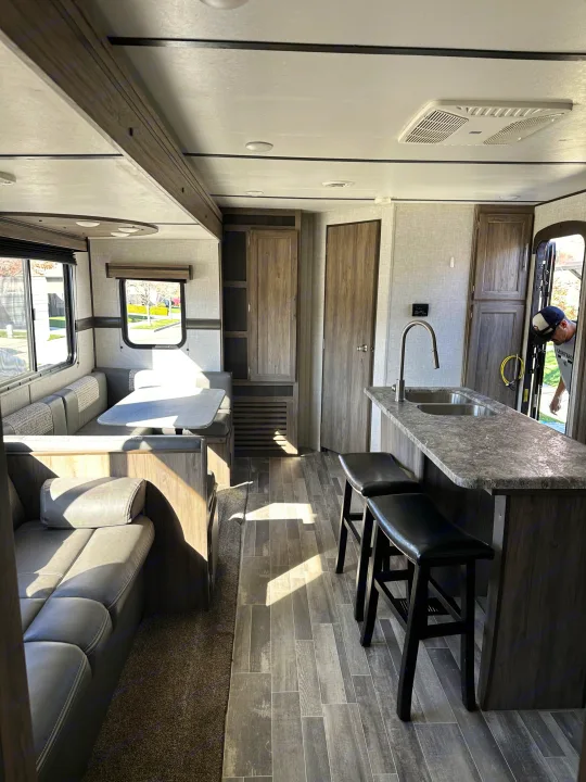 Modern RV rental interior featuring a kitchen island with stools, a dining booth, and a comfortable living area sofa.. Crossroads RV Zinger 2021