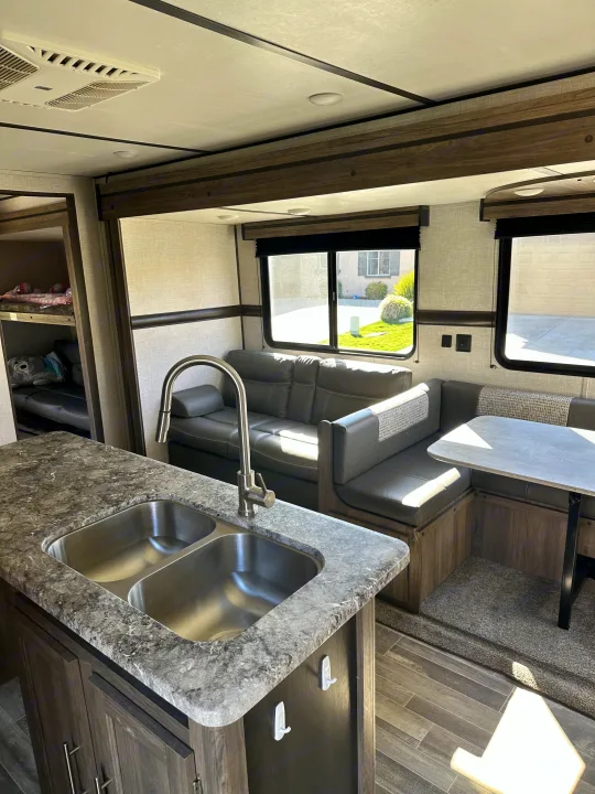 This RV rental offers a kitchen island with double sink, spacious dinette, comfortable sofa, and bunk beds. Ideal travel trailer interior.. Crossroads RV Zinger 2021