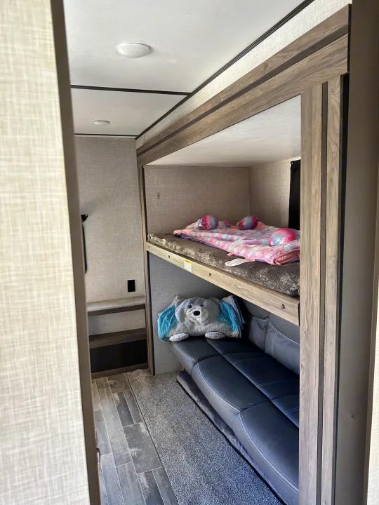 Inside an RV rental: a modern bunk bed setup with a cozy top bunk and a sofa/futon on the bottom level, ready for sleep.. Crossroads RV Zinger 2021