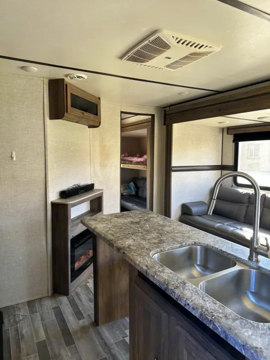 RV rental's inviting interior: kitchen island with double sink, fireplace, comfy sofa, and bunk beds in the back.. Crossroads RV Zinger 2021