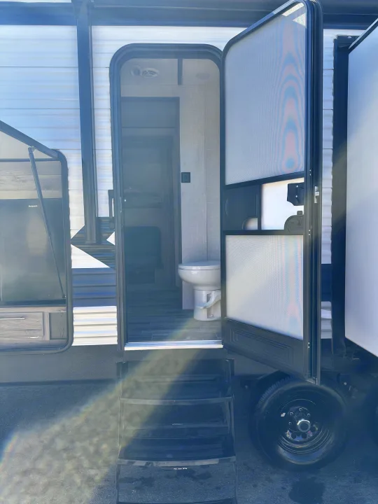 RV rental entrance: an open door reveals pull-out steps, an interior bathroom, and an outdoor kitchen, showcasing comfort for travel.. Crossroads RV Zinger 2021