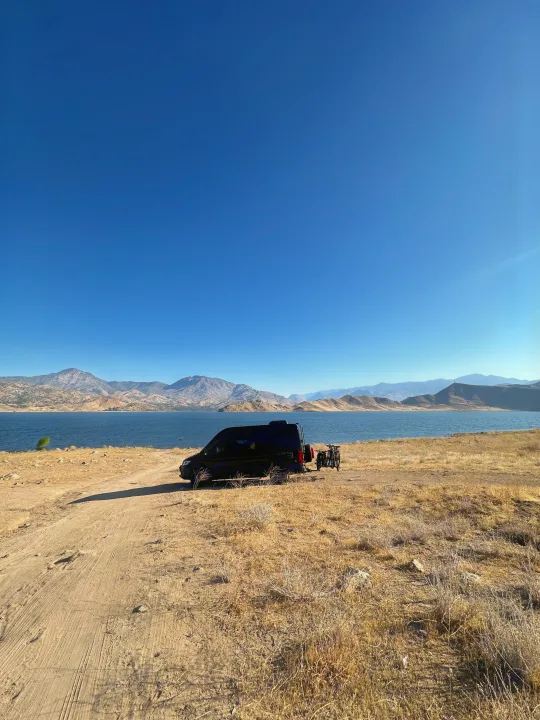 RV rental parked by a serene lake with scenic mountains and bikes, ready for an outdoor adventure.. Mercedez Benz Sprinter 2023