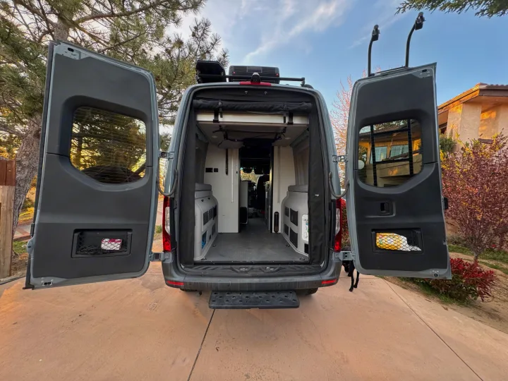 Spacious rear interior of a gray custom camper van with both back doors open, revealing modular storage units. Ideal for rv rental adventures.. Winnebago Revel 2022