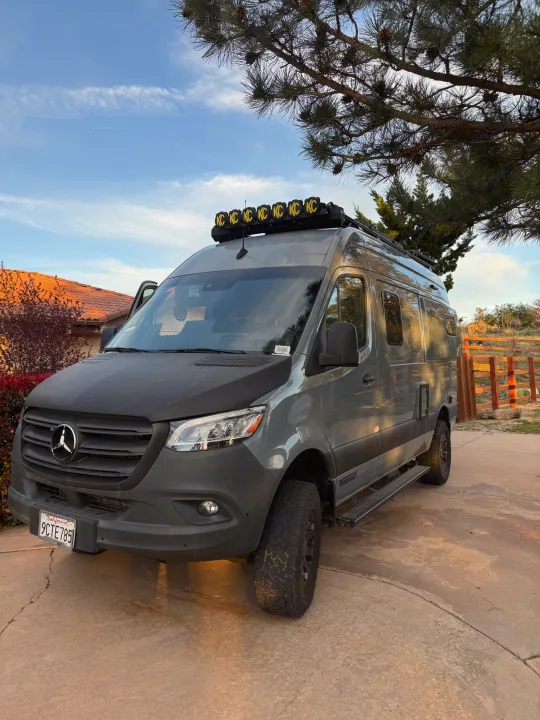 Adventure-ready gray Mercedes Sprinter rv rental, customized for off-road trips with a roof light bar & chunky tires, parked on a driveway.. Winnebago Revel 2022