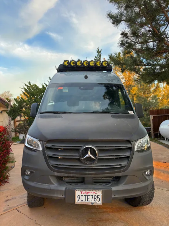 An off-road capable, matte gray Mercedes Sprinter van with KC roof lights, perfect as an rv rental for rugged exploration.. Winnebago Revel 2022