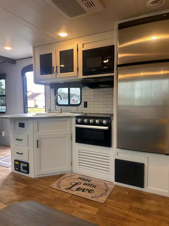 Enjoy this full RV rental kitchen: white cabinets, stainless steel appliances, subway tile backsplash, and wood floors. Ideal for travel!. Keystone RV Hideout 2022