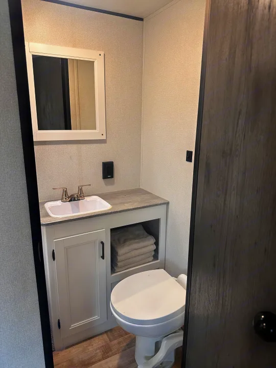 An RV rental bathroom featuring a compact vanity with sink, mirror, and toilet. Folded towels are visible on the shelf.. Keystone RV Hideout 2022