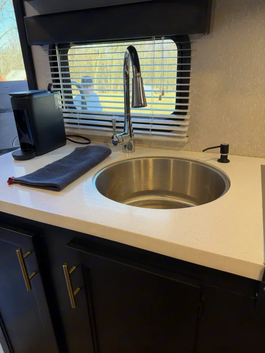 Sleek RV rental kitchen: stainless steel sink, modern faucet, Keurig, soap dispenser, and light speckled countertop by a window.. Forest River Cherokee Wolf Pup Black Label 2021