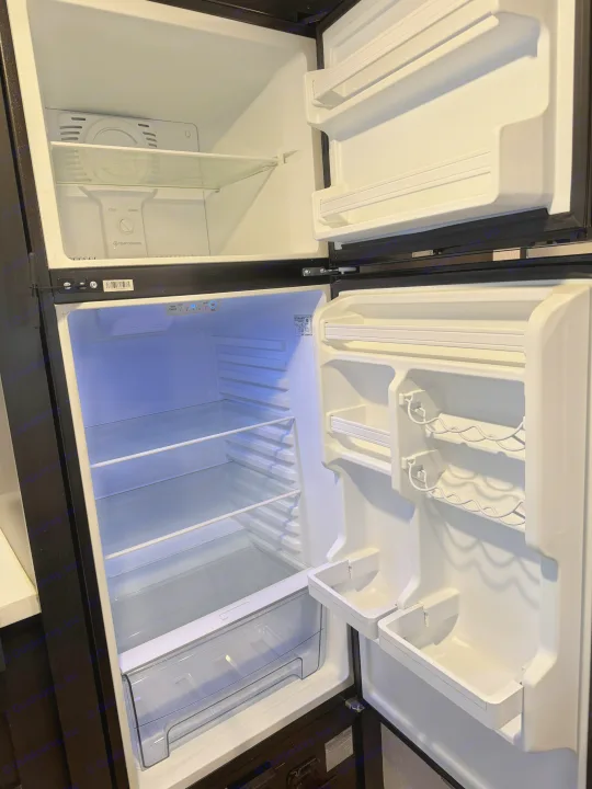 An open, empty **RV rental**'s **refrigerator** and **freezer** compartments, highlighting the clean shelves, door storage, and temperature controls.. Forest River Cherokee Wolf Pup Black Label 2021