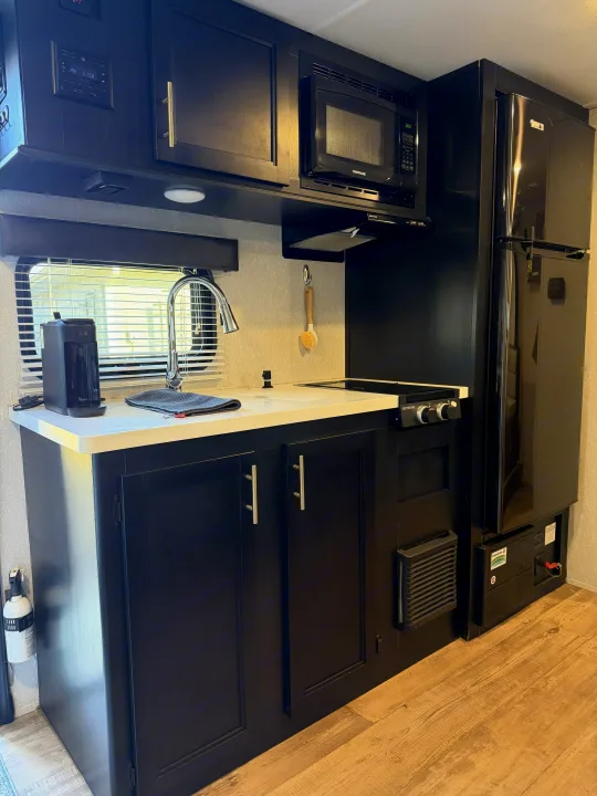 This RV rental features a well-equipped kitchen with sleek black cabinets, white counters, microwave, stovetop, fridge, and sink.. Forest River Cherokee Wolf Pup Black Label 2021