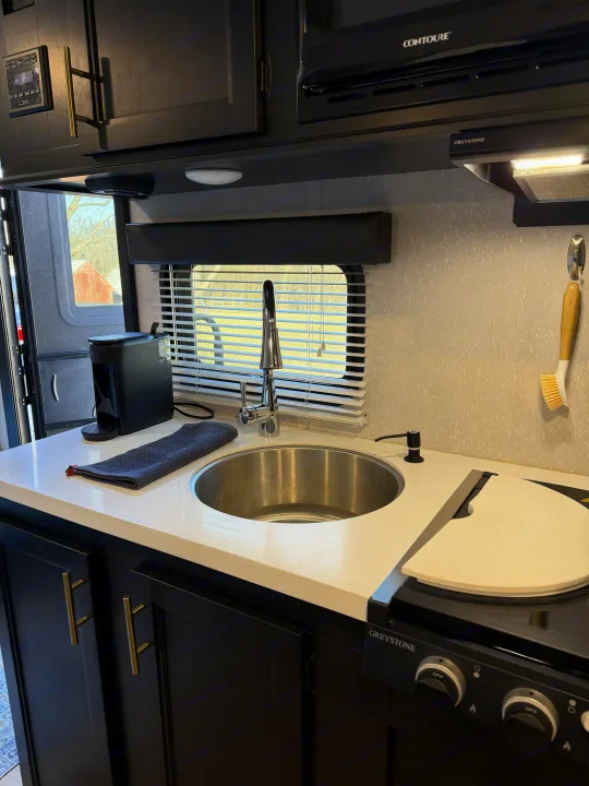 Sleek RV rental kitchen with dark cabinets, bright countertop, sink, stovetop, and coffee maker. Ready for travel!. Forest River Cherokee Wolf Pup Black Label 2021