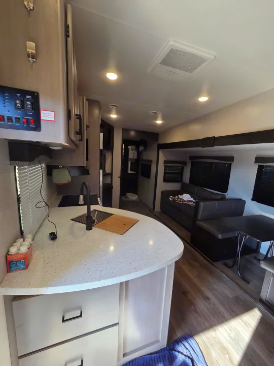 Modern rv rental interior showcasing a bright kitchen with sink, controls panel, and a cozy living area with dinette and sofa.. Starcraft Telluride 2021