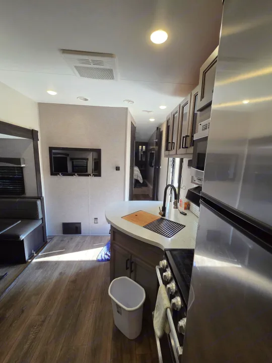 Bright RV rental interior with a modern kitchen island, stainless steel appliances, dining booth, and a wall-mounted TV.. Starcraft Telluride 2021