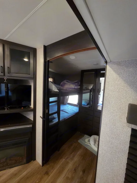 RV rental bunkhouse: features bunk beds, TV, electric fireplace, dark wood cabinetry, and a pet bed on the floor.. Starcraft Telluride 2021