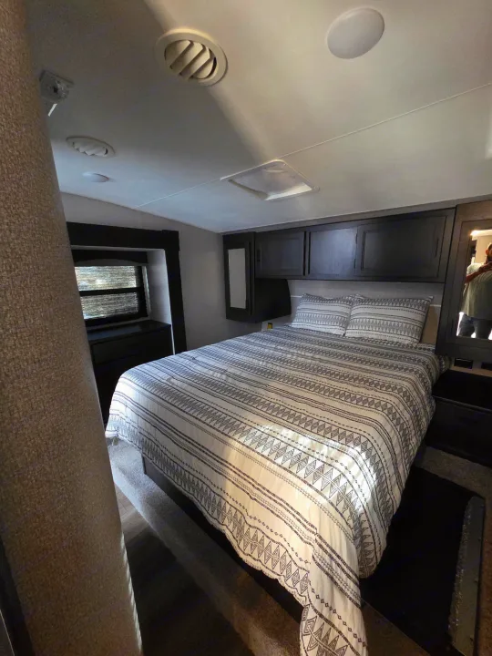 RV rental: A cozy bedroom with a bed, patterned bedding, overhead cabinets, and a window for comfortable stays.. Starcraft Telluride 2021
