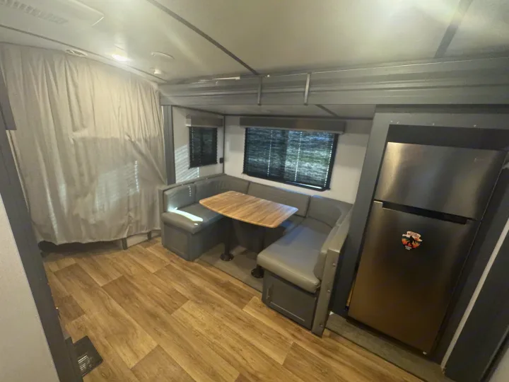 Modern RV rental interior showcasing a U-shaped dining booth, wood-look flooring, and a full-size refrigerator.. Keystone RV Bullet Ultra Lite 2022