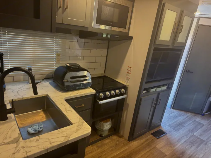 Modern RV rental kitchen: sleek grey cabinets, marble-look counter, sink, Ninja appliance, stove, & microwave.. Keystone RV Bullet Ultra Lite 2022