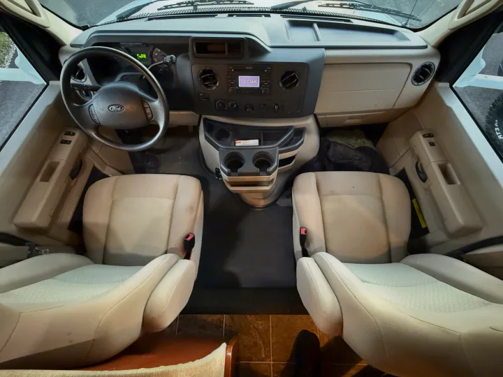 Inside an rv rental: spacious cockpit with a Ford steering wheel, dashboard, dual front seats, and center console.. Thor Freedom Elite 2012