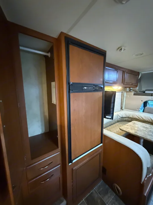 RV rental interior featuring a wood-paneled refrigerator, wardrobe with drawers, and comfortable dinette seating with table.. Thor Freedom Elite 2012
