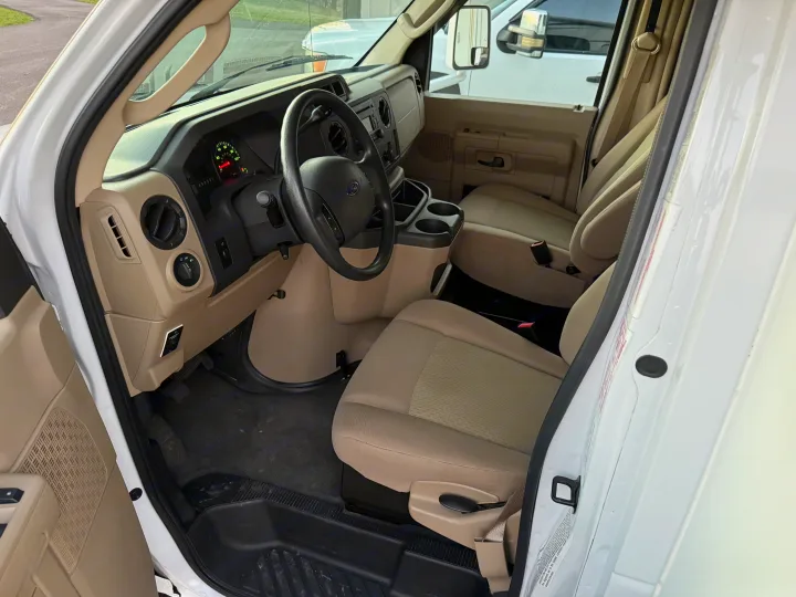 Interior of an RV rental van, showing the driver's cockpit with a black steering wheel, dashboard, and beige front seats.. Thor Freedom Elite 2012
