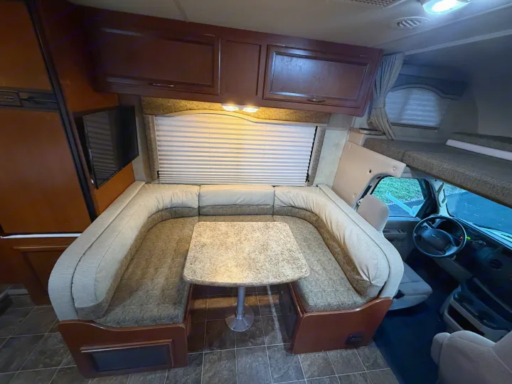 Spacious RV rental interior featuring a U-shaped dinette, overhead cabinets, TV, and a cab-over bunk.. Thor Freedom Elite 2012