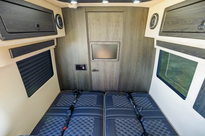 This RV rental features dual black quilted seats with seatbelts, overhead storage, and a rear screen, ready for travel adventures.. OGV Luxury Coach V-Cruise 2026