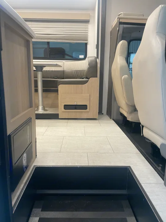 RV rental interior. Low angle shows dining booth, table, and front seats, with a large black floor step in foreground.. Coachmen Leprechaun 2026