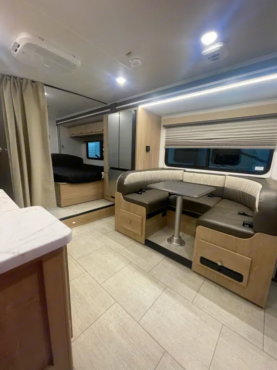 This rv rental offers a comfortable modern interior, with a U-shaped dinette, refrigerator, and a cozy bed area behind a curtain.. Coachmen Leprechaun 2026