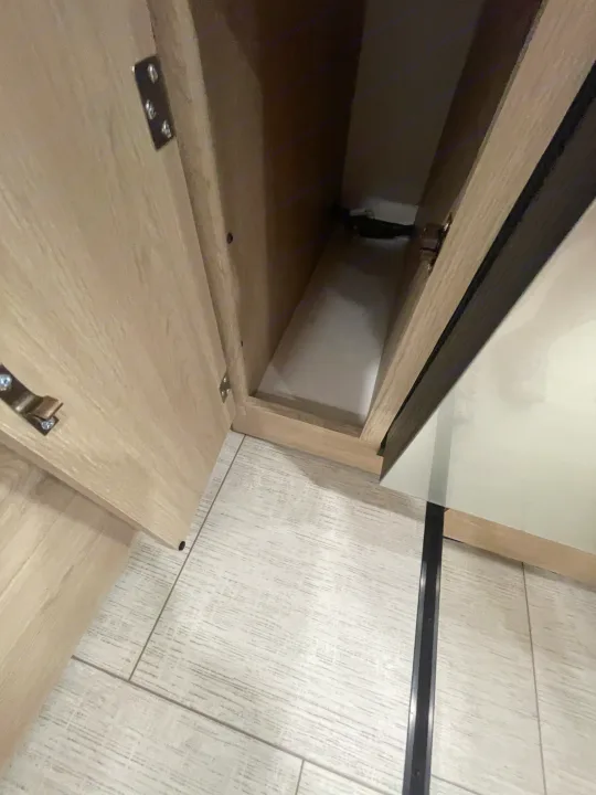 Open light wood cabinet in an RV rental, featuring hinges, deep storage, and a matching light-toned floor. Organize essentials.. Coachmen Leprechaun 2026