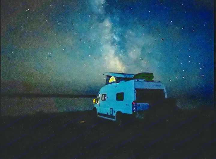 An RV rental camper van parked under a stunning Milky Way sky at night, with interior lights glowing. Ideal for celestial escapes.. Winnebago Solis 2022