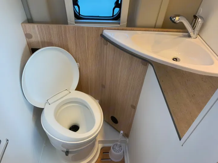 Compact RV rental bathroom with a white toilet (lid up) and a space-saving corner sink featuring a chrome faucet.. Sunlight Cliff 600 2023