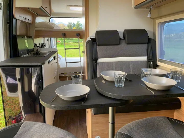 Spacious RV rental interior featuring a modern kitchenette, comfortable dining area set for four, and bunk beds with a view outside.. Sunlight Cliff 600 2023