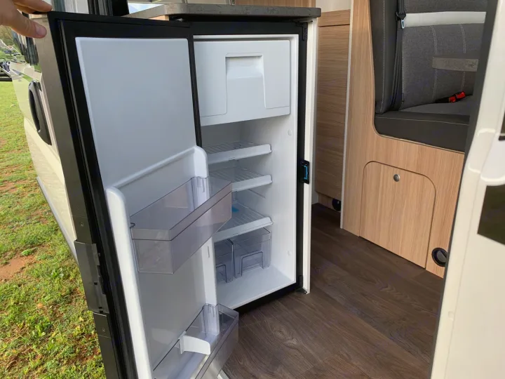 Clean, open refrigerator in this modern rv rental camper van, showing empty shelves and storage. Ready for your trip!. Sunlight Cliff 600 2023