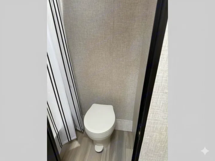 Compact RV rental bathroom with a white toilet, gray walls, wood-look floor, and a white and black striped shower curtain.. Starcraft Autumn Ridge 2026