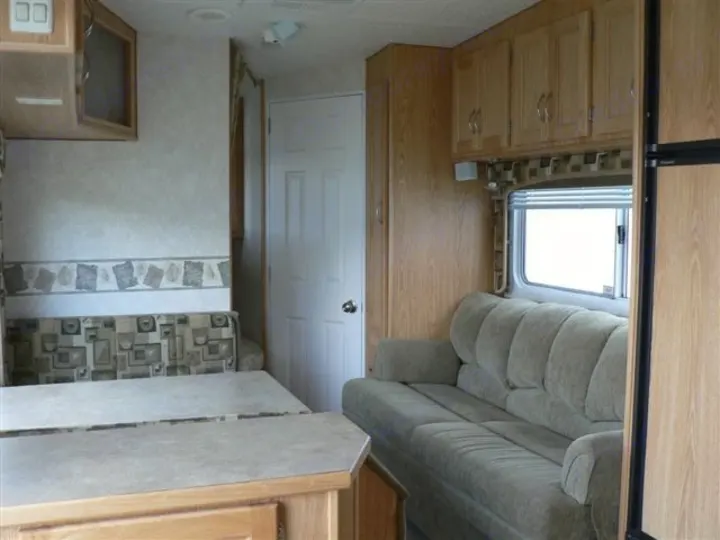 Interior of an RV rental showing a dinette, patterned booth seating, a comfy sofa, and overhead storage cabinets.. Frontier FW255 2012