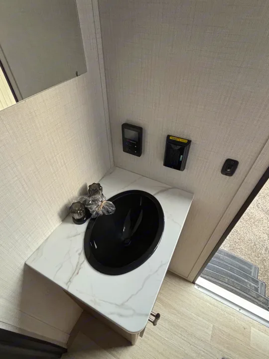 Modern RV rental bathroom vanity, with a black sink, white marble-look counter, and wall controls. Faucet still wrapped.. Keystone Springdale 261BHC 2026