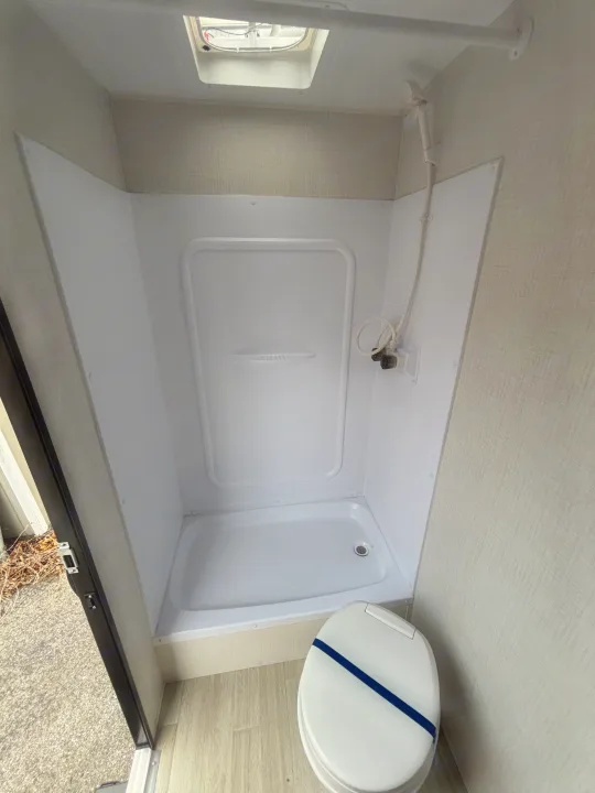 Compact RV rental bathroom with a white shower stall, toilet, light walls, and overhead vent, ready for your travels.. Keystone Springdale 261BHC 2026