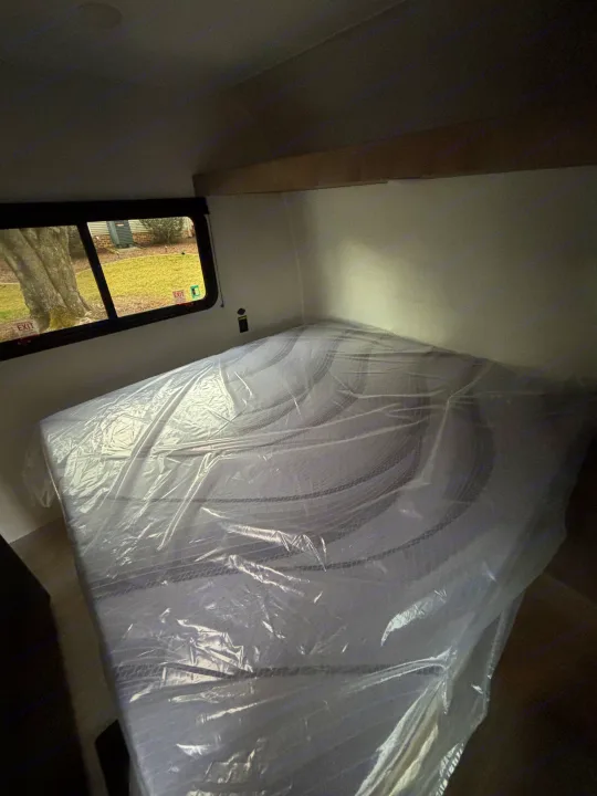 RV rental bedroom with a new, plastic-covered mattress and an outdoor view through the window.. Keystone Springdale 261BHC 2026