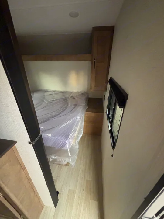 Cozy RV rental bedroom with a plastic-covered bed, built-in cabinets, and a window with a blind. Perfect for compact living.. Keystone Springdale 261BHC 2026