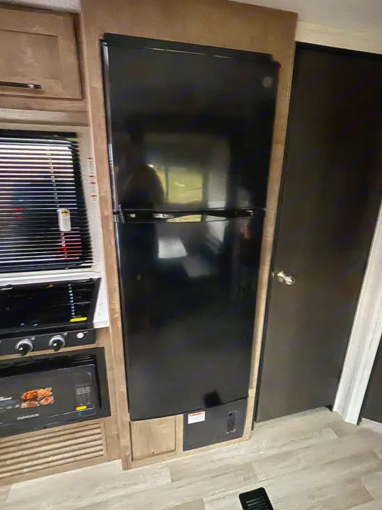 This RV rental kitchen features a tall black refrigerator, stove, oven, and window with blinds.. Keystone Springdale 261BHC 2026