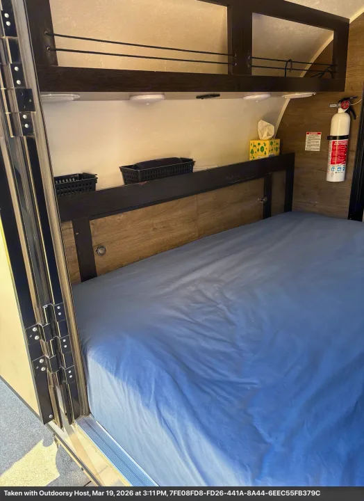 Inside an RV rental: a bed with blue sheets, overhead storage, and a fire extinguisher for a safe trip.. Braxton Creek Free Solo 2022